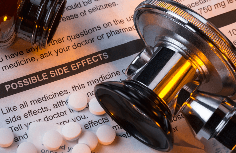 A stethoscope laid over a side effect warning sheet with pills.