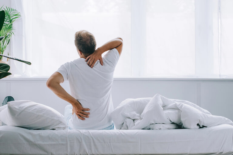 Man experiencing back and neck pain getting out of bed.