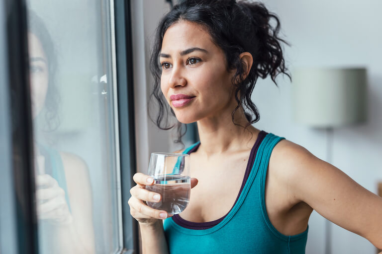 Women drinking a glass of water looking out a window.